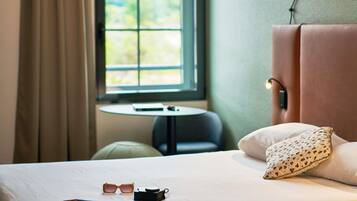 Een hotelkamer met een bed, een klein tafeltje en een raam met gordijnen.