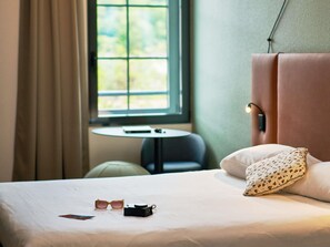 Una habitación de hotel con cama, una mesita y una ventana con cortinas.
