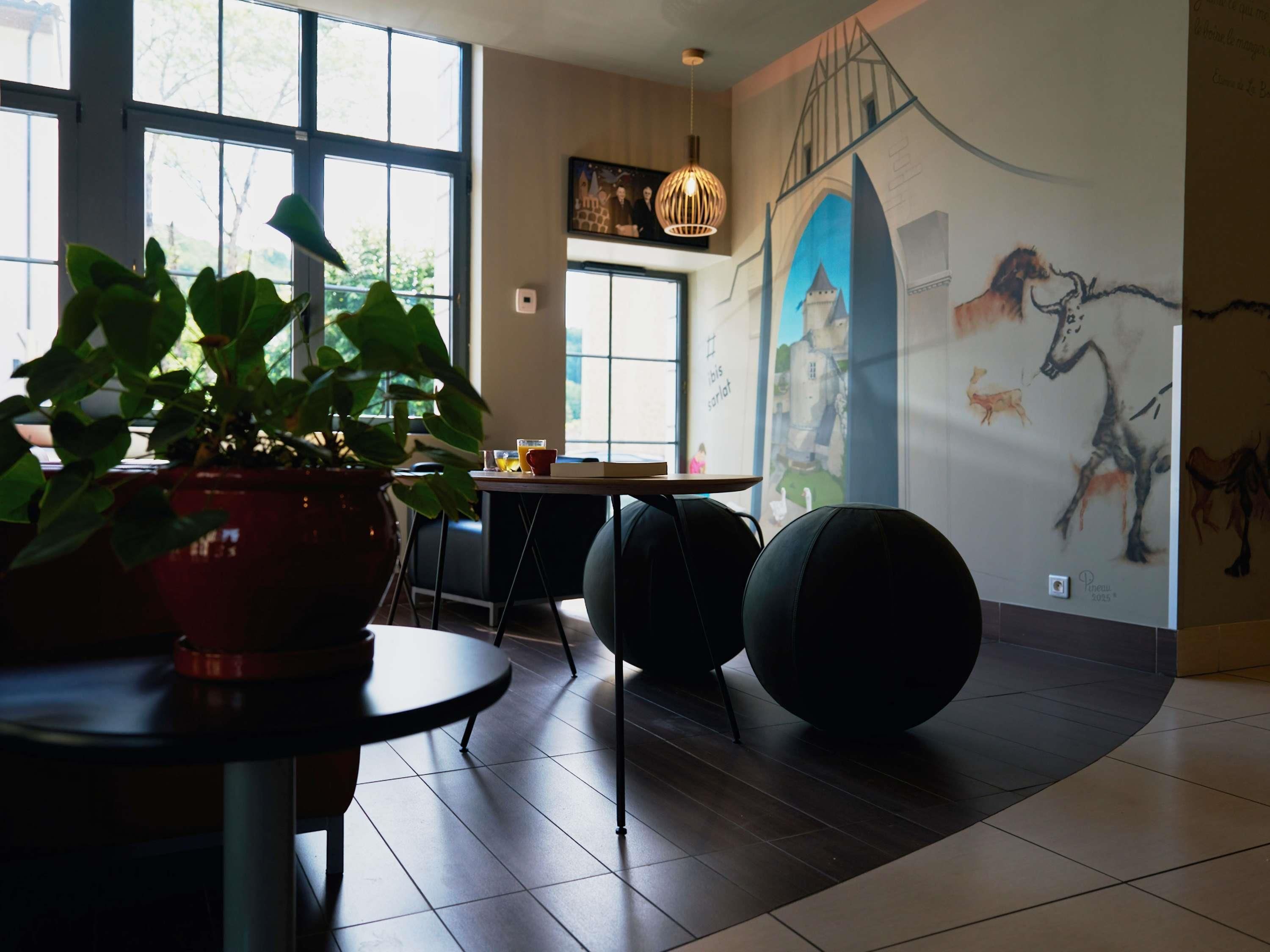 A modern interior with a dining area, a large potted plant, a wall mural, and a hanging light fixture.