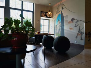 A modern interior with a dining area, a large potted plant, a wall mural, and a hanging light fixture.