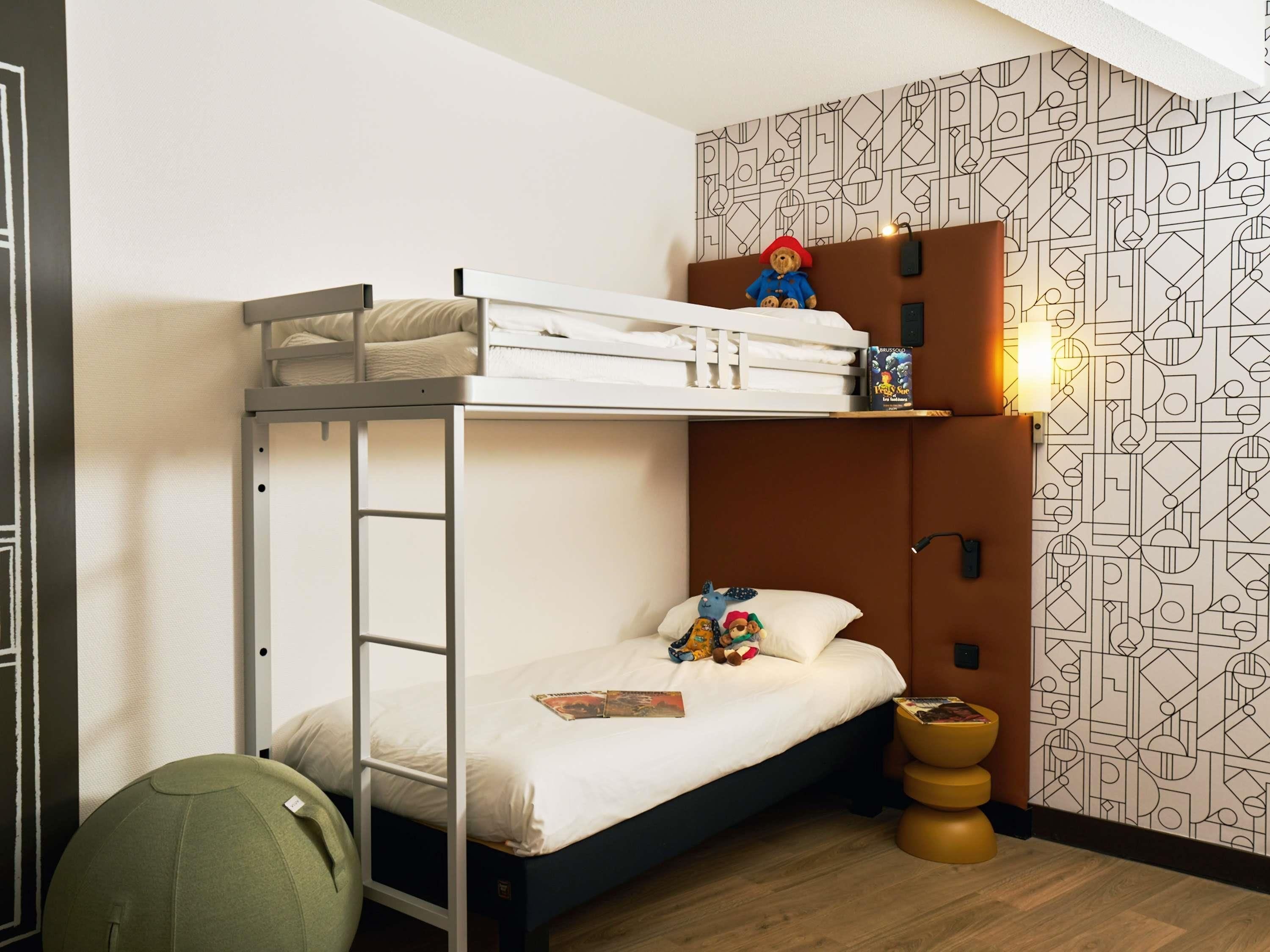 A bunk bed with a ladder, a small bedside table, and a wall with geometric wallpaper.