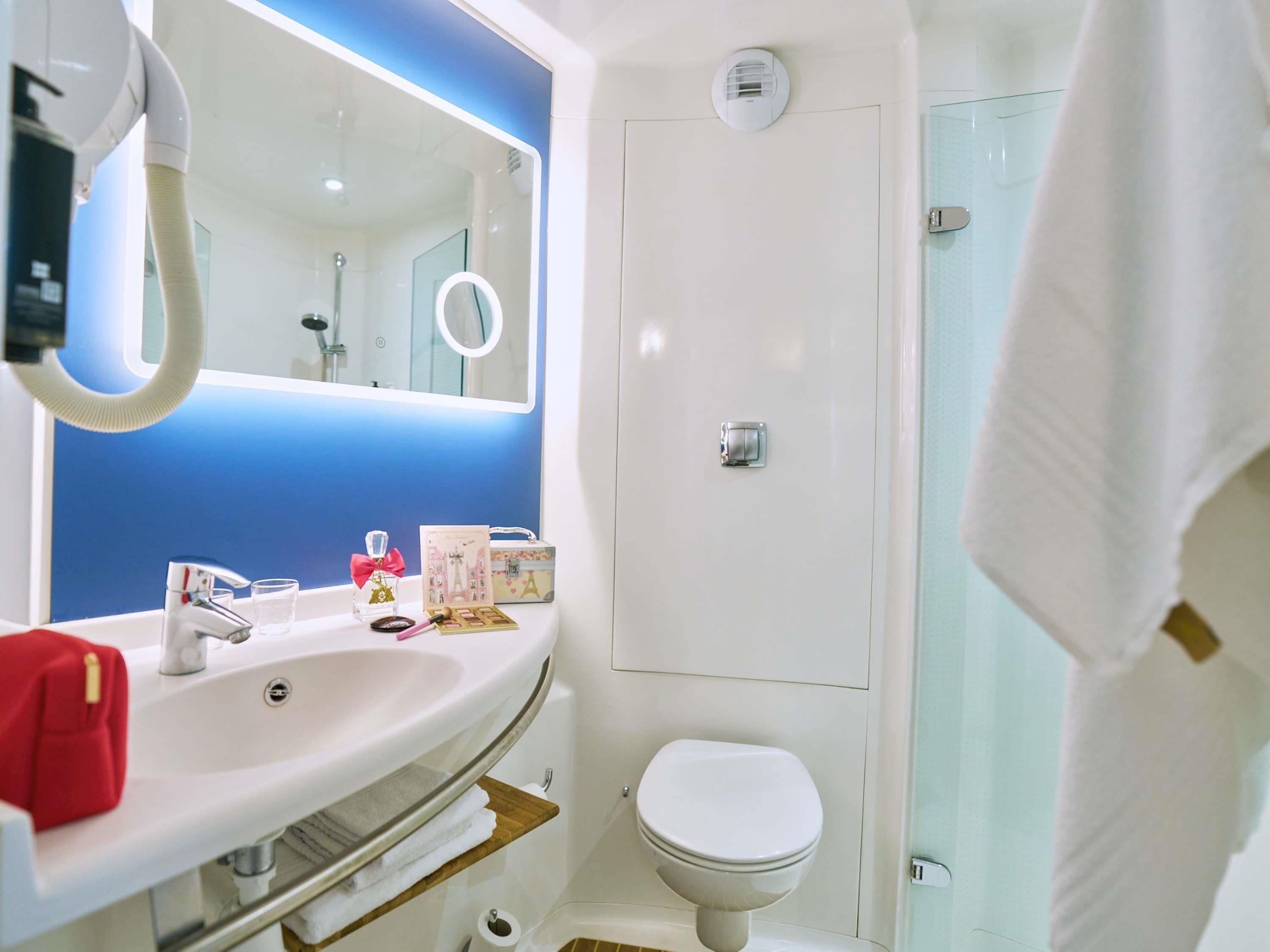 Ein Badezimmer mit weißem Waschbecken, Spiegel und Toilette. Ein Handtuchhalter, eine Duschvorhang und ein Duschkopf sind vorhanden.