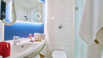 Ein Badezimmer mit weißem Waschbecken, Spiegel und Toilette. Ein Handtuchhalter, eine Duschvorhang und ein Duschkopf sind vorhanden.