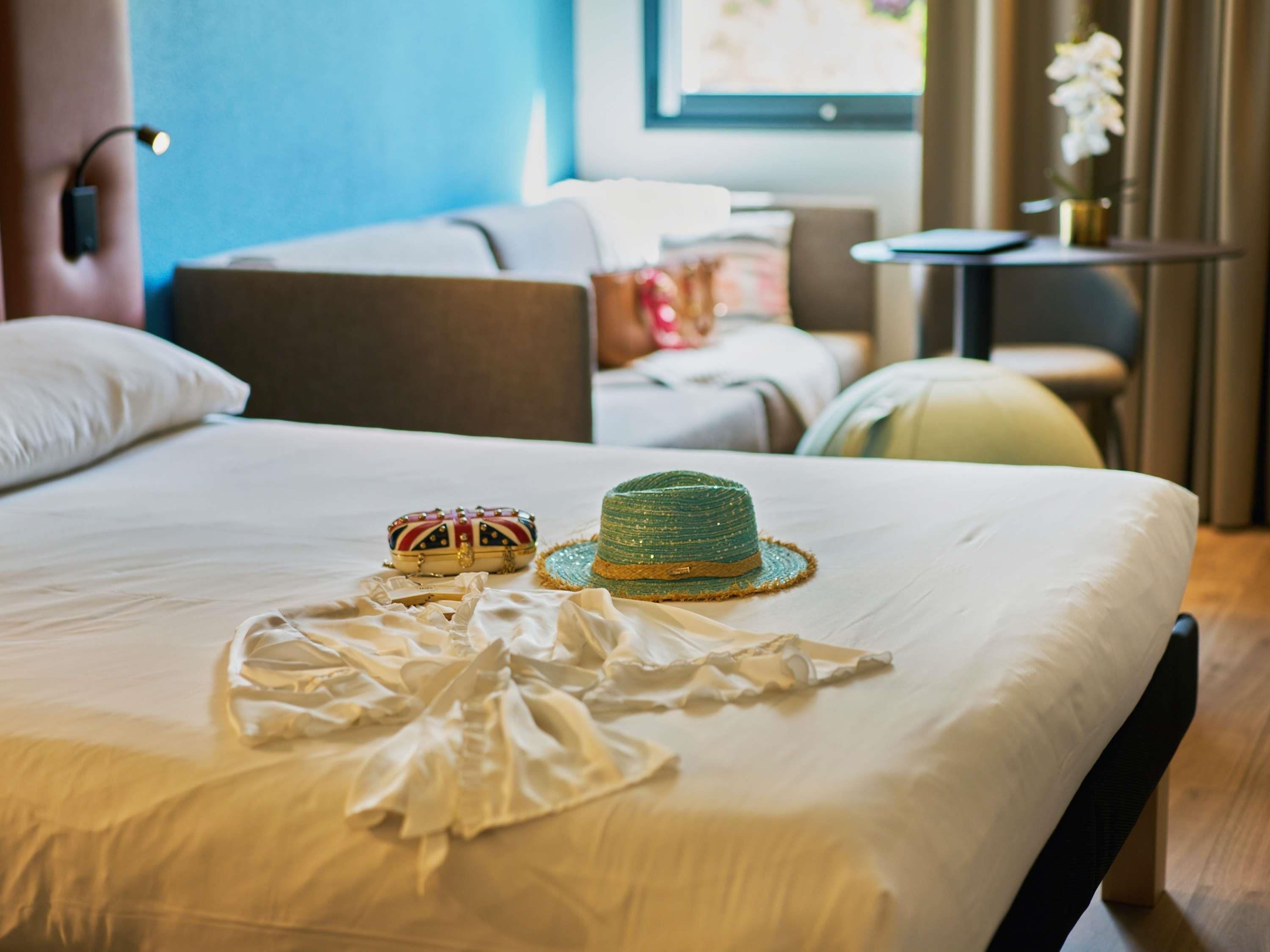 A neatly made bed with a white bedsheet, a green hat, and a decorative bag on the bed.