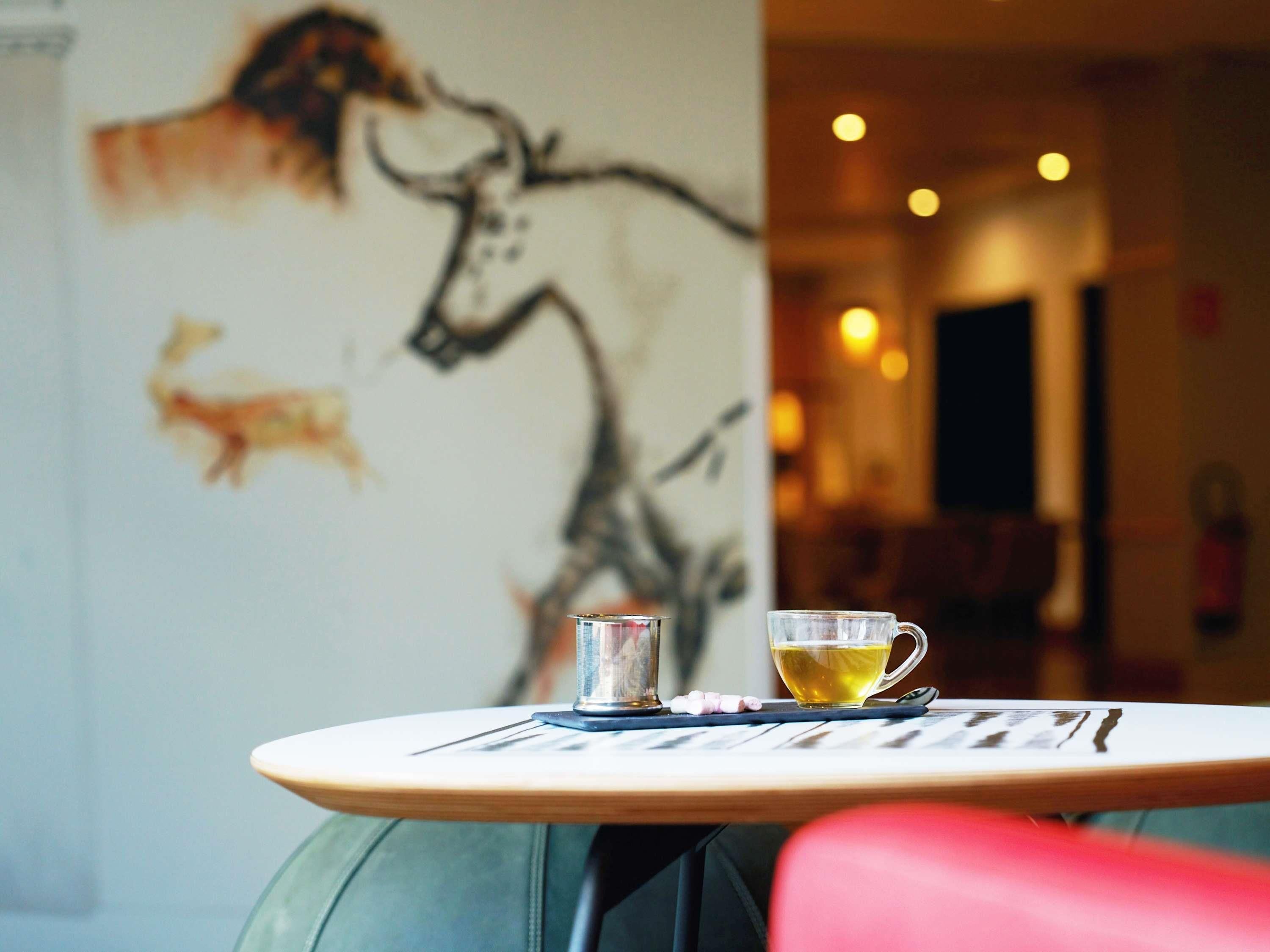 Una mesa con una taza de té, un vaso y algunos comprimidos, con un mural en la pared de fondo.