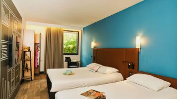 Hotelkamer met twee bedden, een bureau, een stoel, een garderobe en een raam met uitzicht op groen.