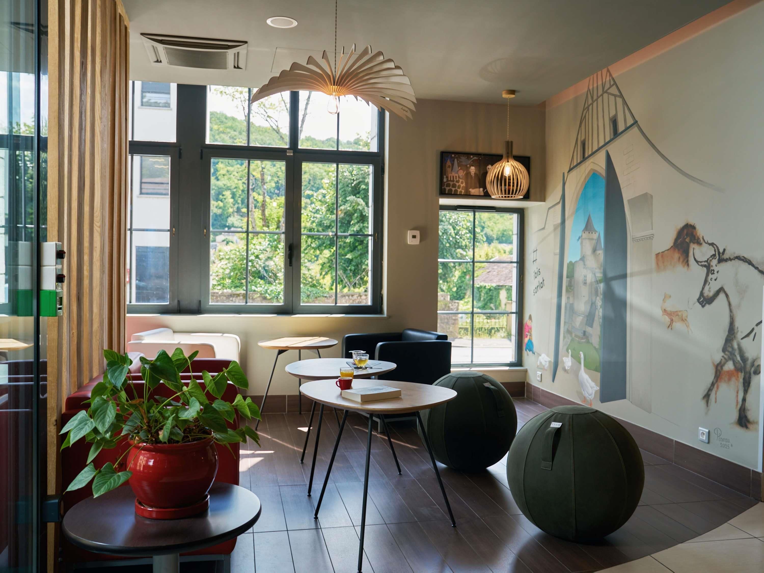 A modern interior with large windows, a mural, and a mix of seating options including a round table and bean bag.