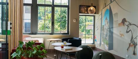A modern interior with large windows, a mural, and a mix of seating options including a round table and bean bag.