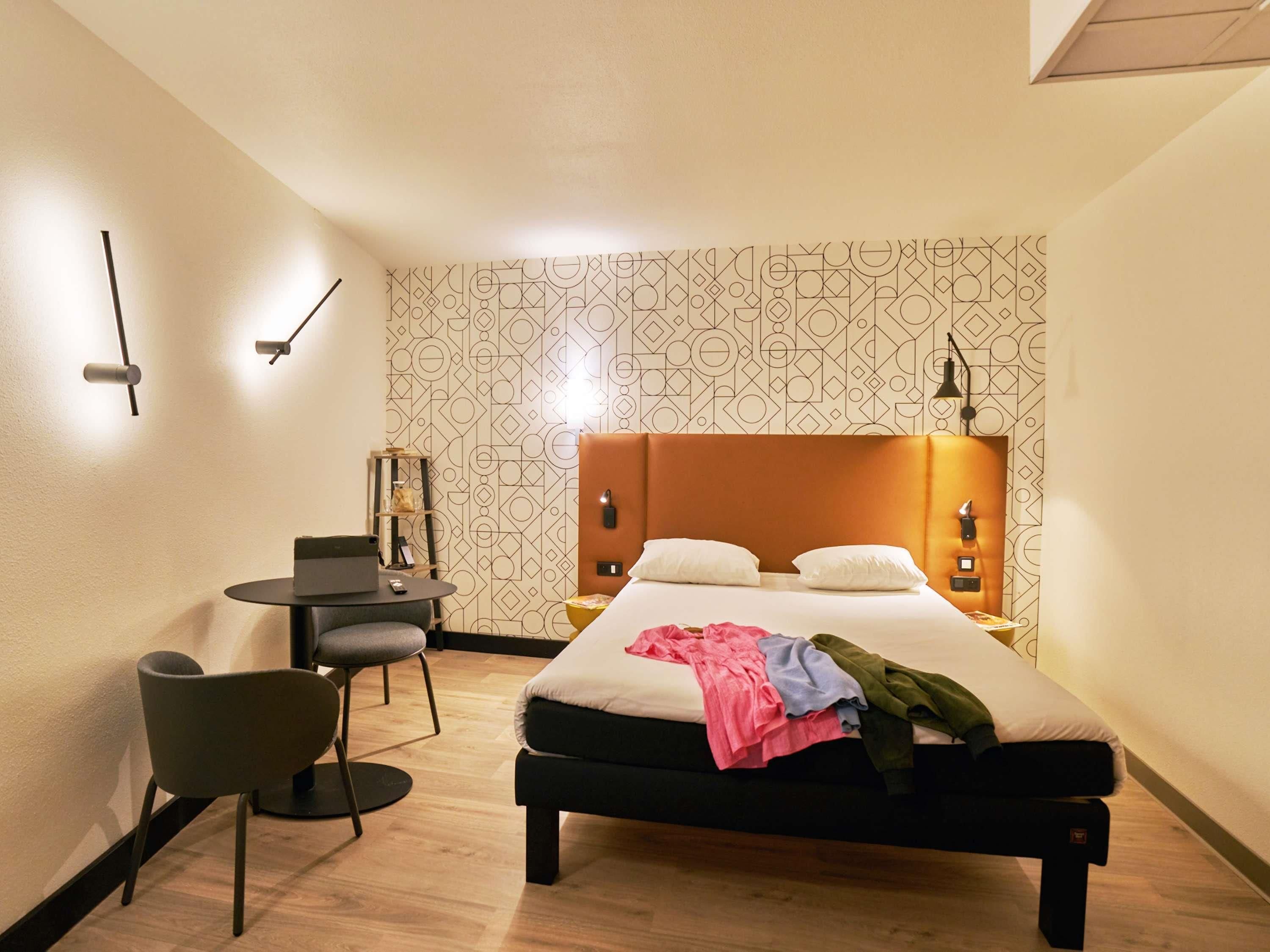 Een hotelkamer met een bed, nachtkastjes, een bureau met stoel en een wandlamp.