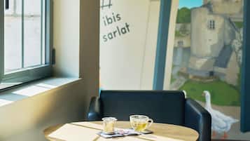Une table avec une tasse de thé et un verre d’eau, une chaise et un mur orné d’une fresque représentant un château.