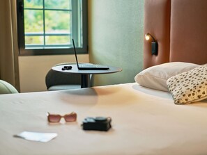 A neatly made bed with a laptop on a small table beside it, a pair of sunglasses, and a camera on the bed. - ibis Sarlat (Sarlat-la-Canéda)