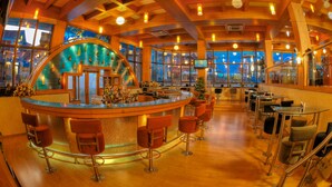A bar area with a curved counter, multiple stools, and a large window offering a view of the outside. - Aldovia Resort & Convention (Bengaluru)