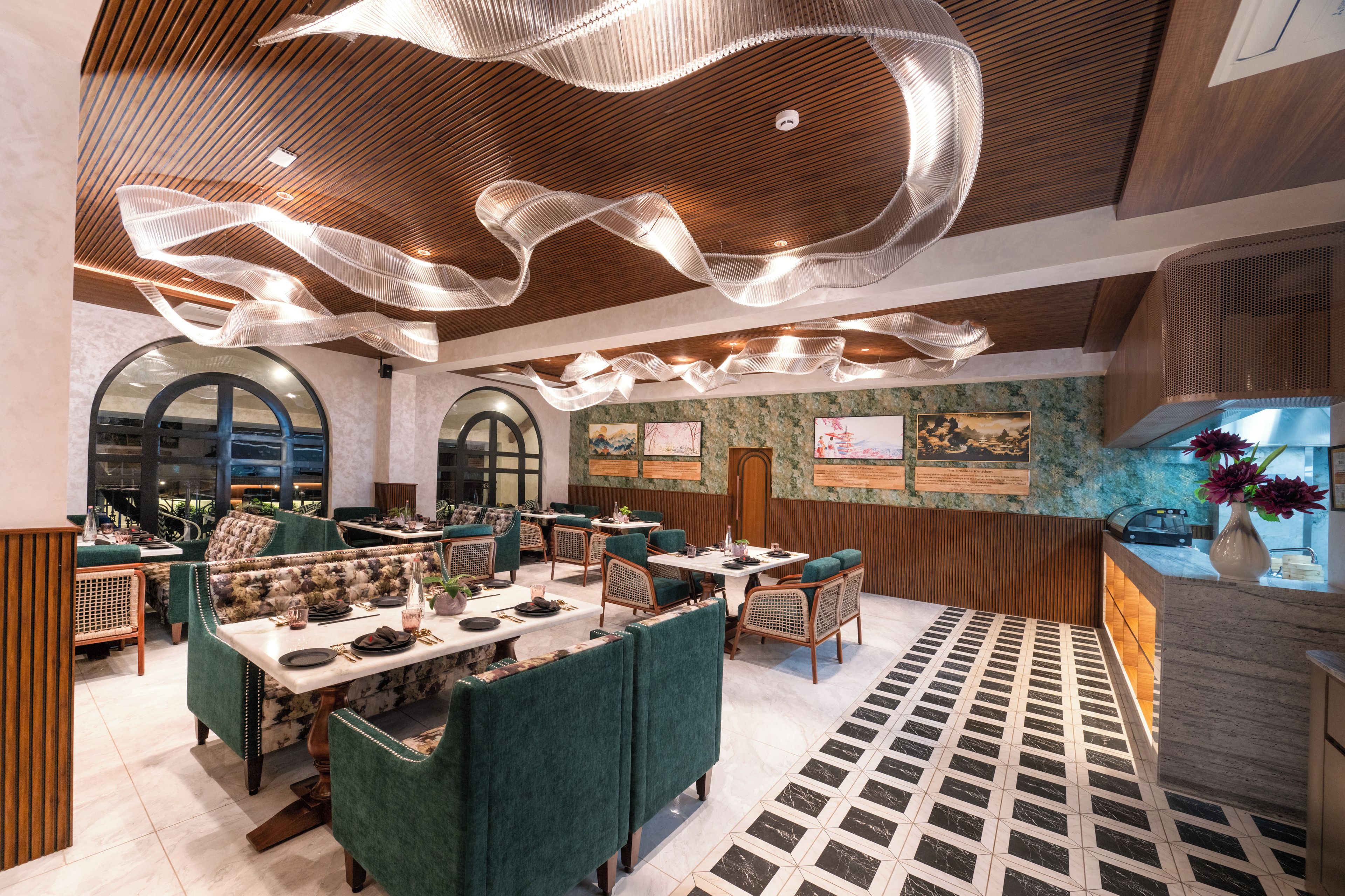 A restaurant with green upholstered booths, a patterned floor, and a ceiling with hanging light fixtures.