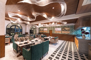 A restaurant with green upholstered booths, a patterned floor, and a ceiling with hanging light fixtures. - Aldovia Resort & Convention (Bengaluru)