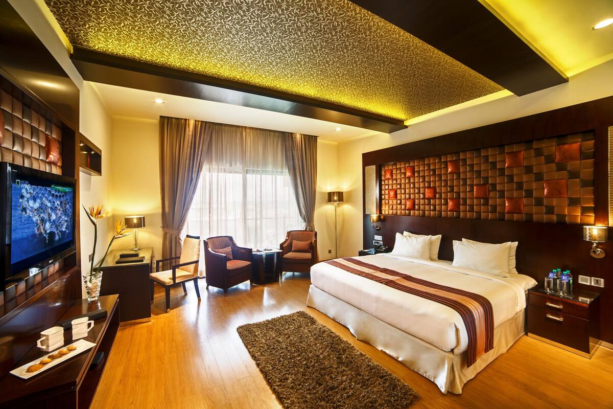 A hotel room with a large bed, a TV, a desk with a chair, and a sofa.