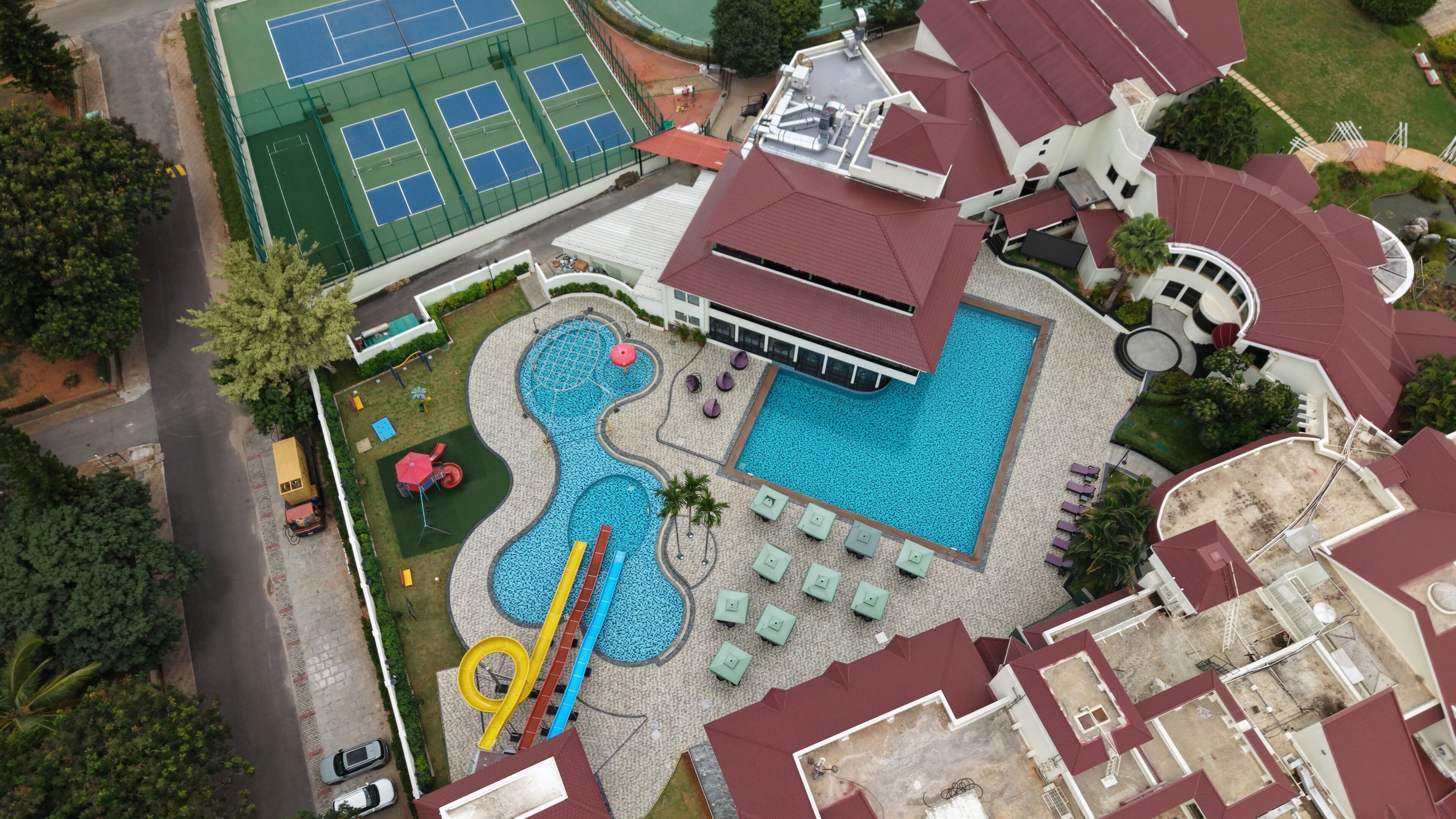 An aerial view of a residential property with a swimming pool, tennis courts, and a landscaped garden.