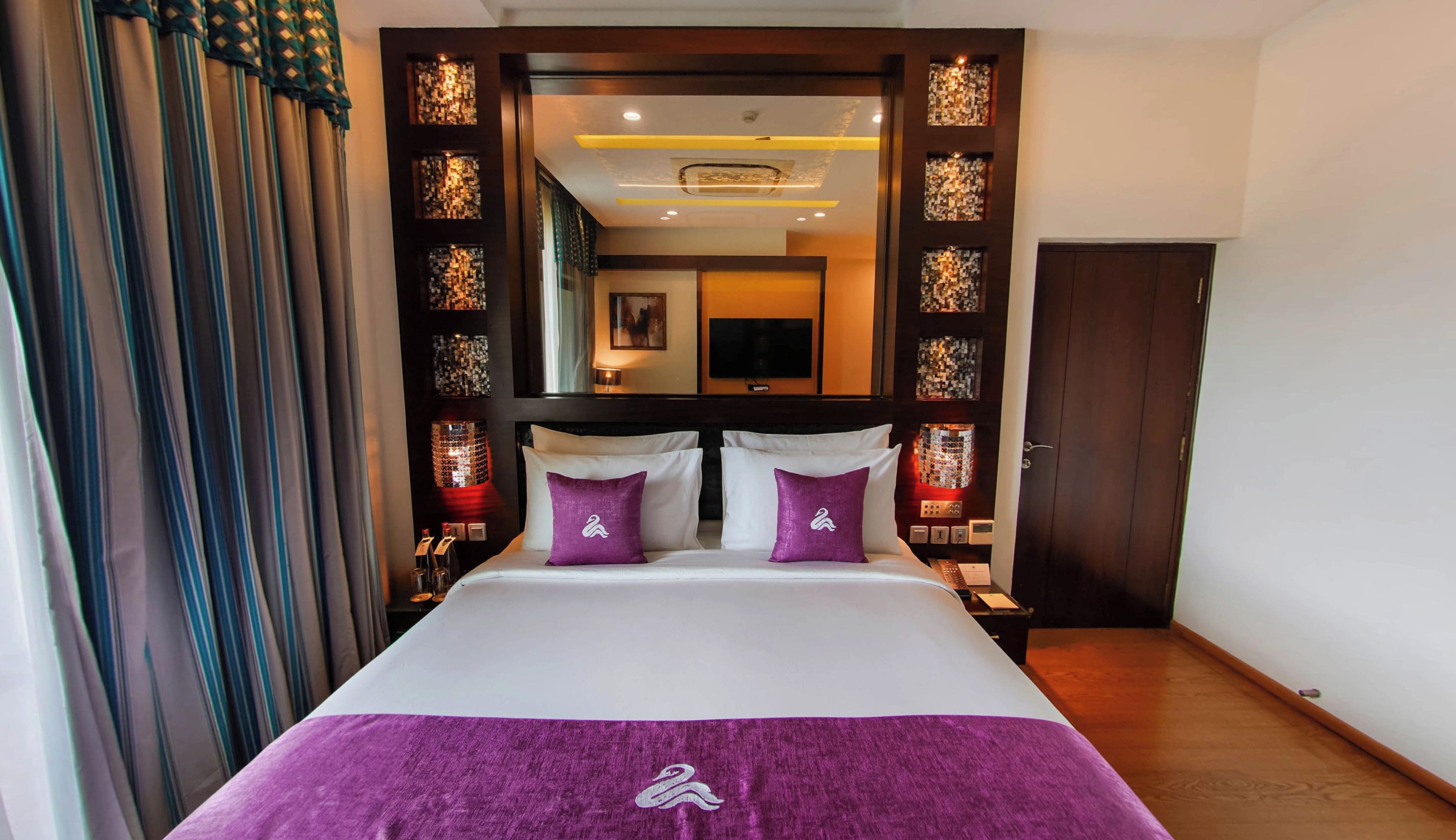 A hotel room with a bed, a nightstand, a mirror, and a door.