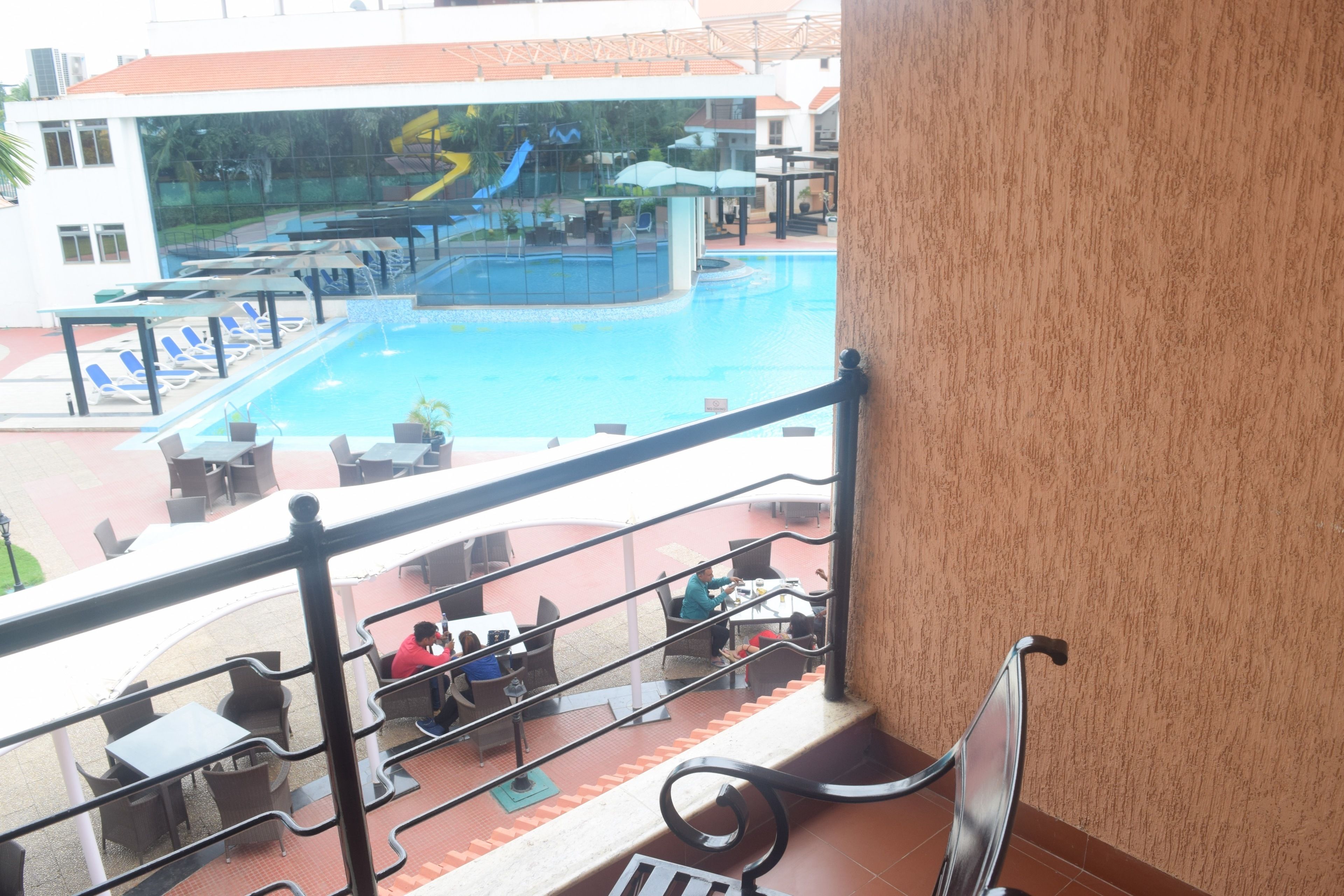 A pool area with lounge chairs and tables, a slide, and a view of the pool from a balcony.