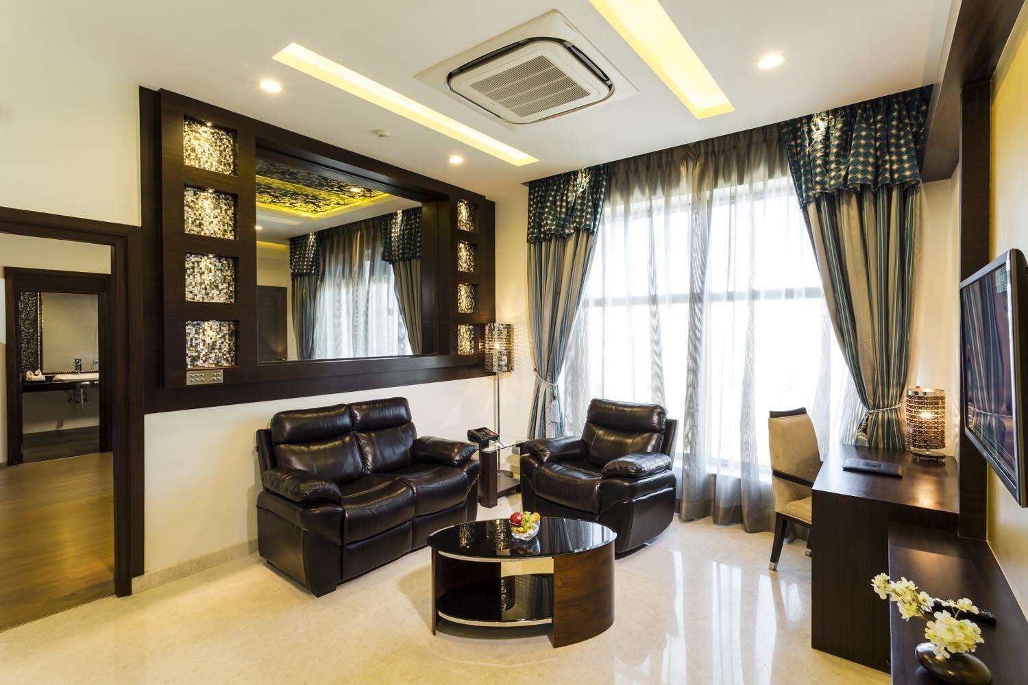 A modern living room with a black leather sofa, a matching armchair, and a coffee table. There is a large mirror on the wall, a flat-screen TV, and a decorative vase on a side table.