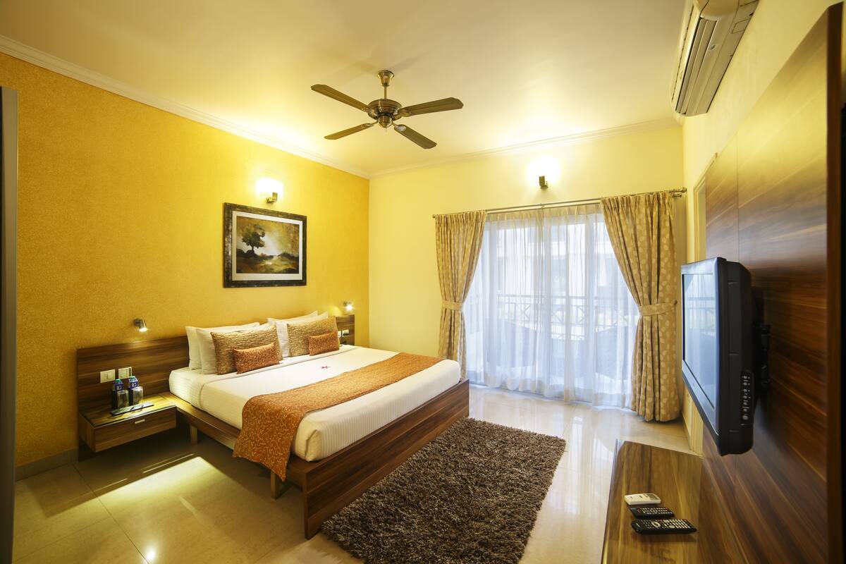 A hotel room with a bed, a television, a ceiling fan, and a window with curtains.