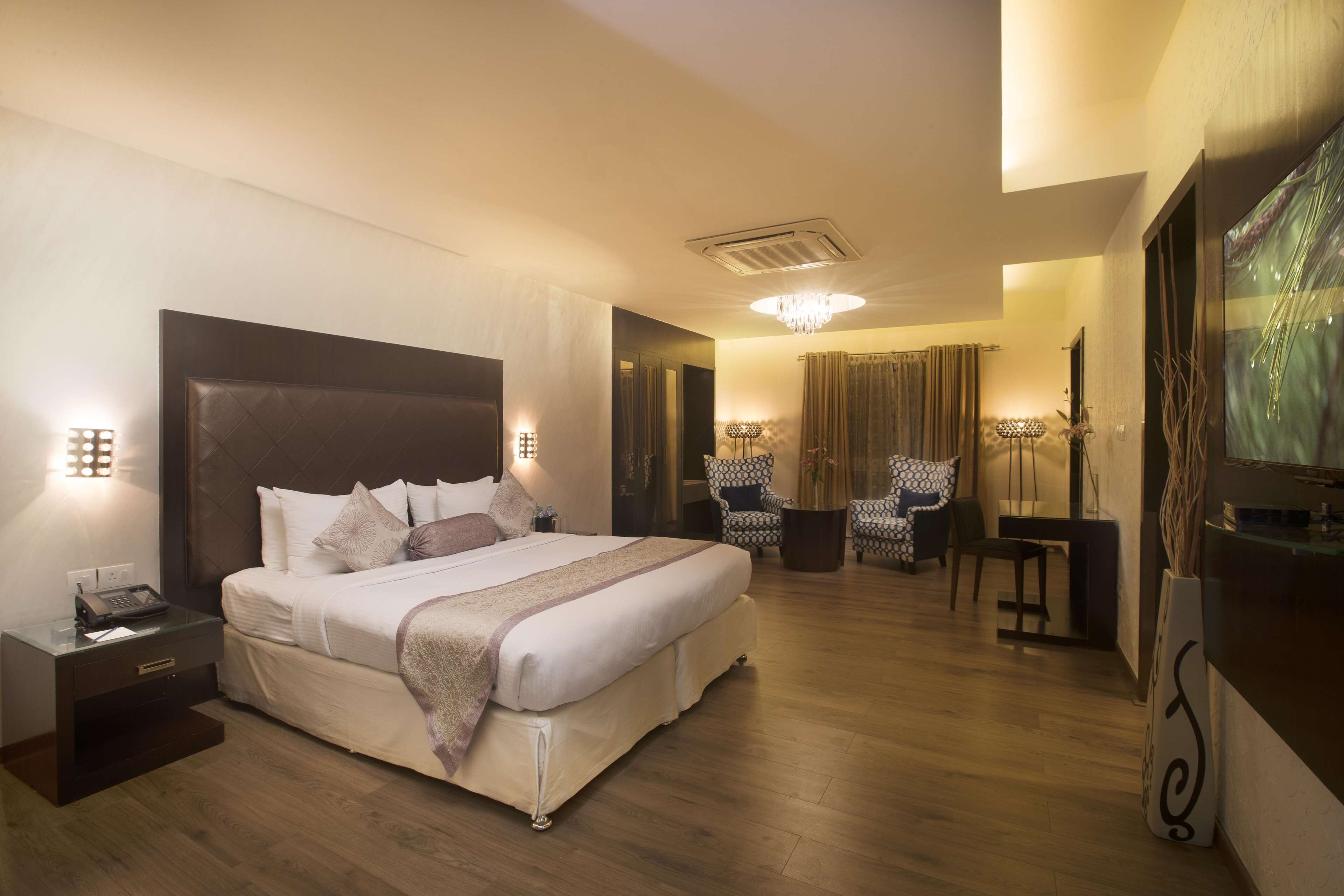 A hotel room with a large bed, bedside tables, a desk, chairs, and a TV.