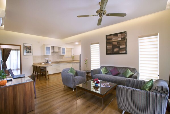 A modern living room with a dining area, a kitchen in the background, and a ceiling fan.