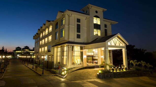 A large, multi-story hotel with a grand entrance, multiple windows, and a well-lit facade. - Aldovia Resort & Convention (Bengaluru)