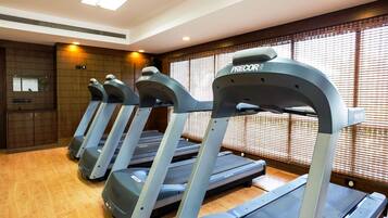 File di tapis roulant in palestra, con pavimento in legno e ampie finestre.