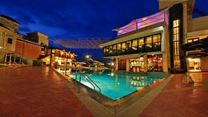 A nighttime swimming pool area with a modern building, a covered seating area, and a bar. - Aldovia Resort & Convention (Bengaluru)
