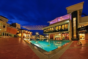Uma área de piscina à noite, com um edifício moderno, um espaço de estar coberto e um bar.