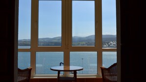 Una habitación con un gran ventanal que da a una masa de agua y colinas distantes.