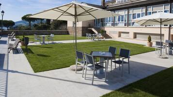 Un patio con mobiliario exterior, incluidas mesas y sillas, y grandes sombrillas que brindan sombra.