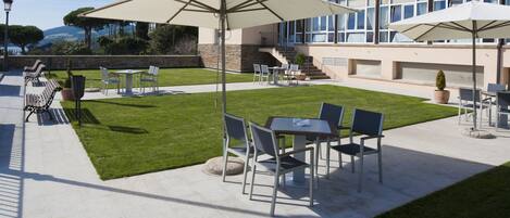 A patio area with outdoor seating, including tables and chairs, and large umbrellas providing shade.