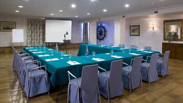 Un salón de conferencias con una larga mesa, sillas, una pantalla de proyector y un adorno con timón de barco.
