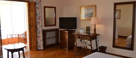 Habitación de hotel con cama, escritorio con lámpara, televisión, silla, armario y un espejo grande.