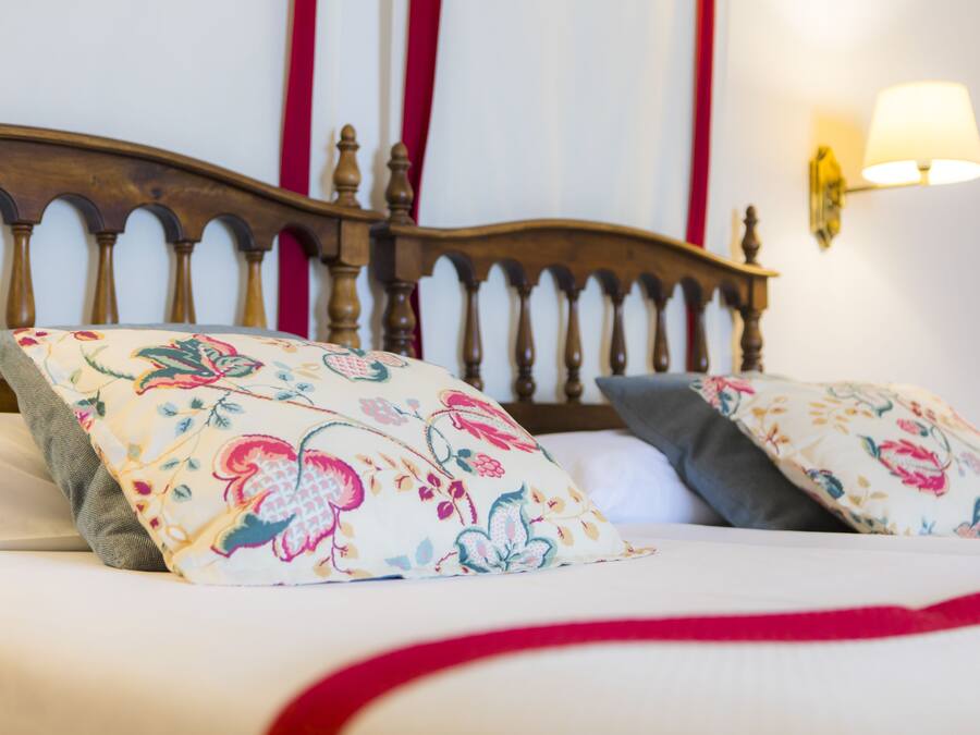 Una cama con almohadas estampadas con motivos florales, un cabecero de madera y una lámpara de pared.