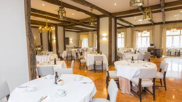 Un vaste espace dédié à la salle à manger, avec plusieurs tables rondes dressées pour le repas, recouvertes de nappes blanches et agrémentées de chaises.