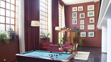 Una mesa de billar en una sala con ventanas amplias, paredes rojas y cuadros enmarcados.