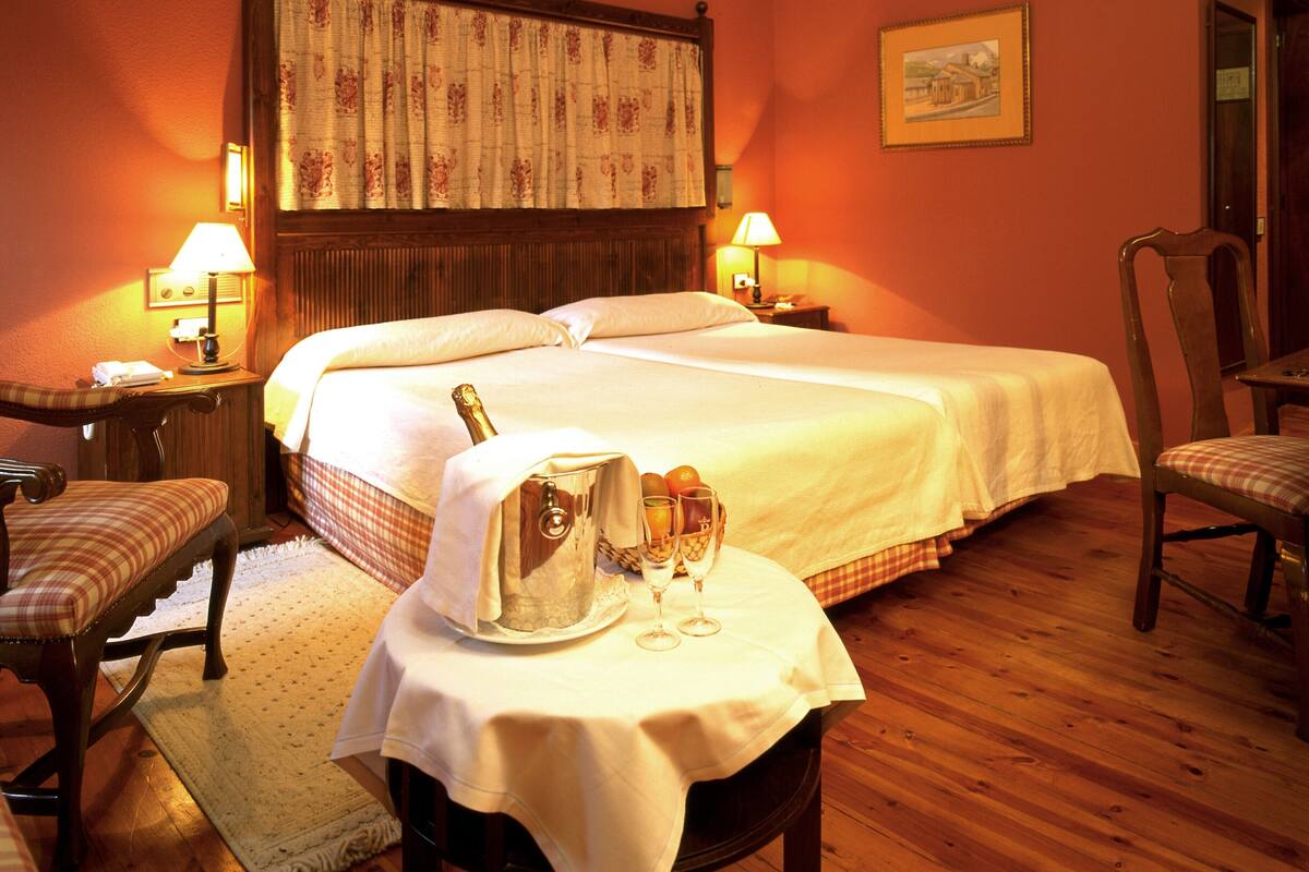 A hotel room with two beds, wooden flooring, a wooden headboard, a framed picture on the wall, and two bedside lamps.