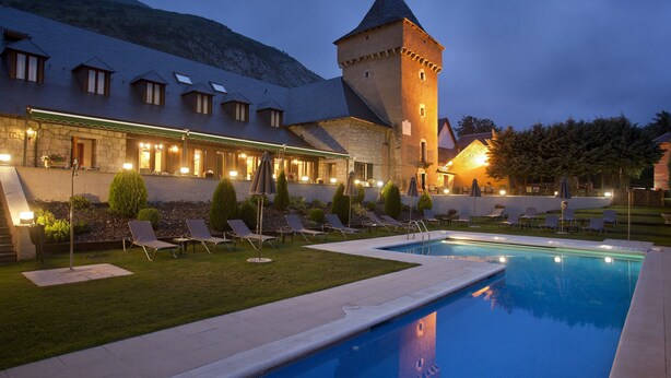 Un hotel con piscina, sillas de descanso y una torre.