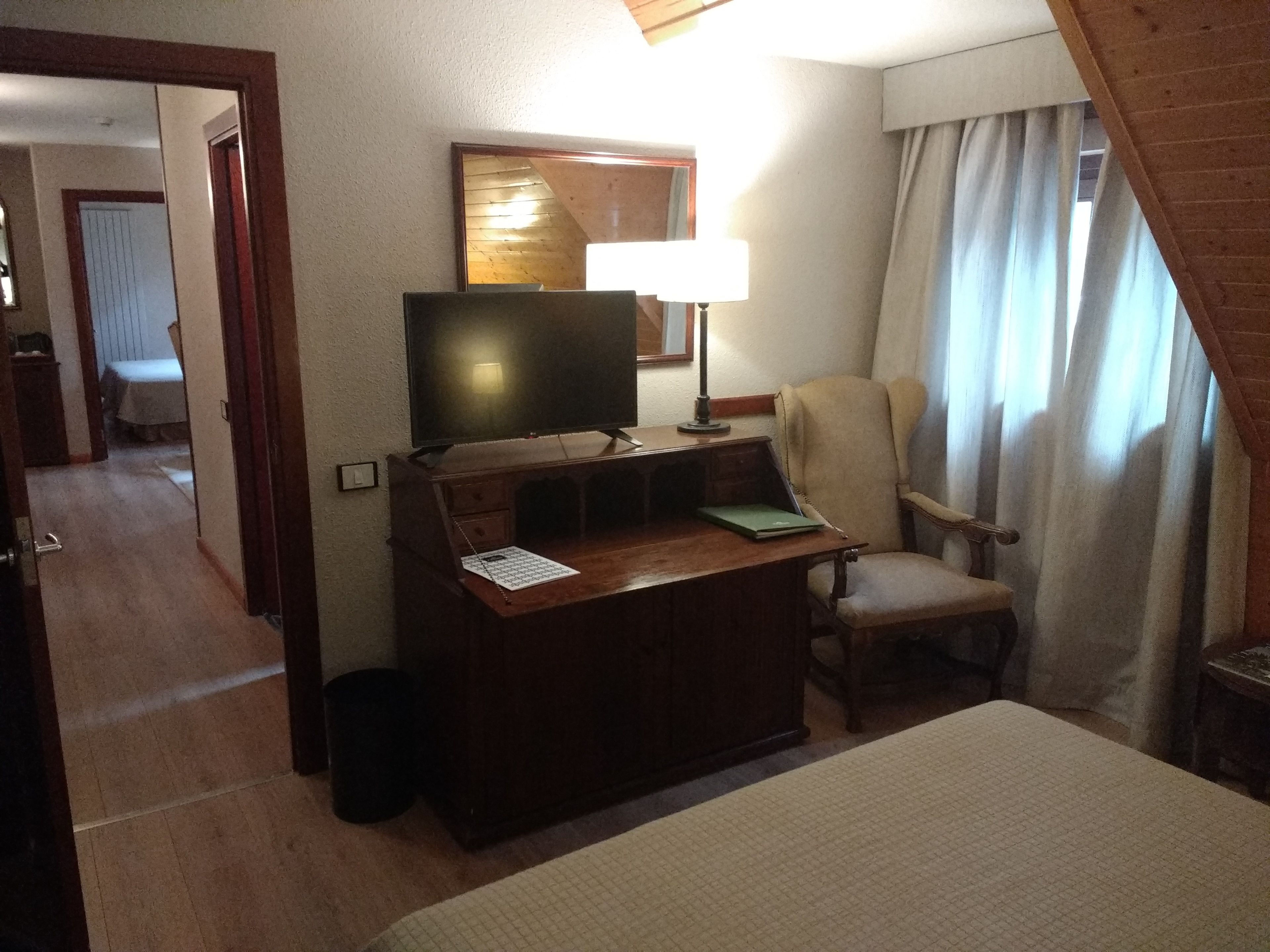 Une chambre d’hôtel avec un lit, un bureau doté d’une lampe, une chaise, un téléviseur et un miroir au mur.