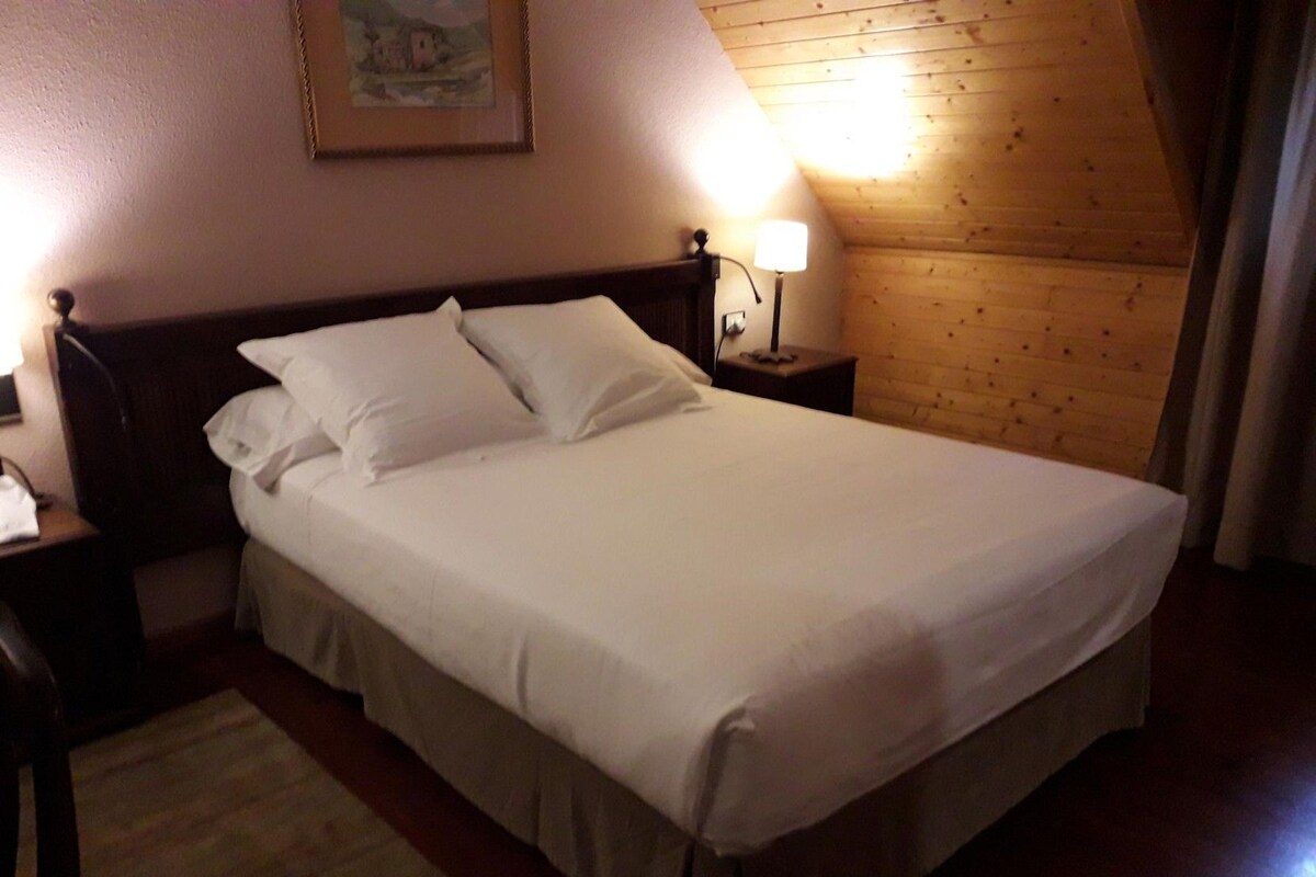 A neatly made bed in a room with wooden walls and a framed picture on the wall.