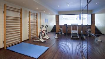 A gym with wooden floors, exercise equipment, and a blue mat.