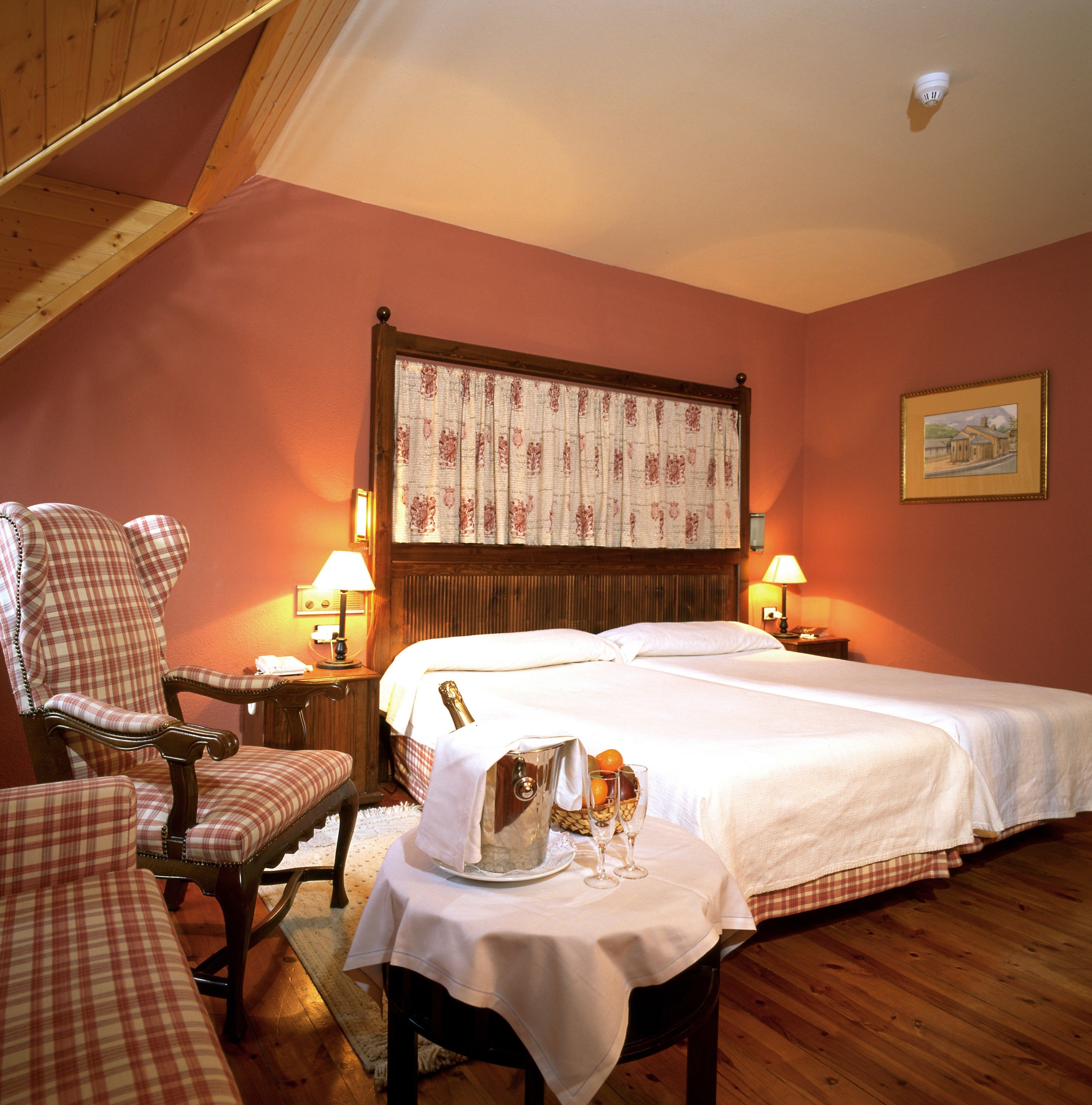 Une chambre avec deux lits, une chaise, une table avec une bouteille et des verres, et un tableau accroché au mur.