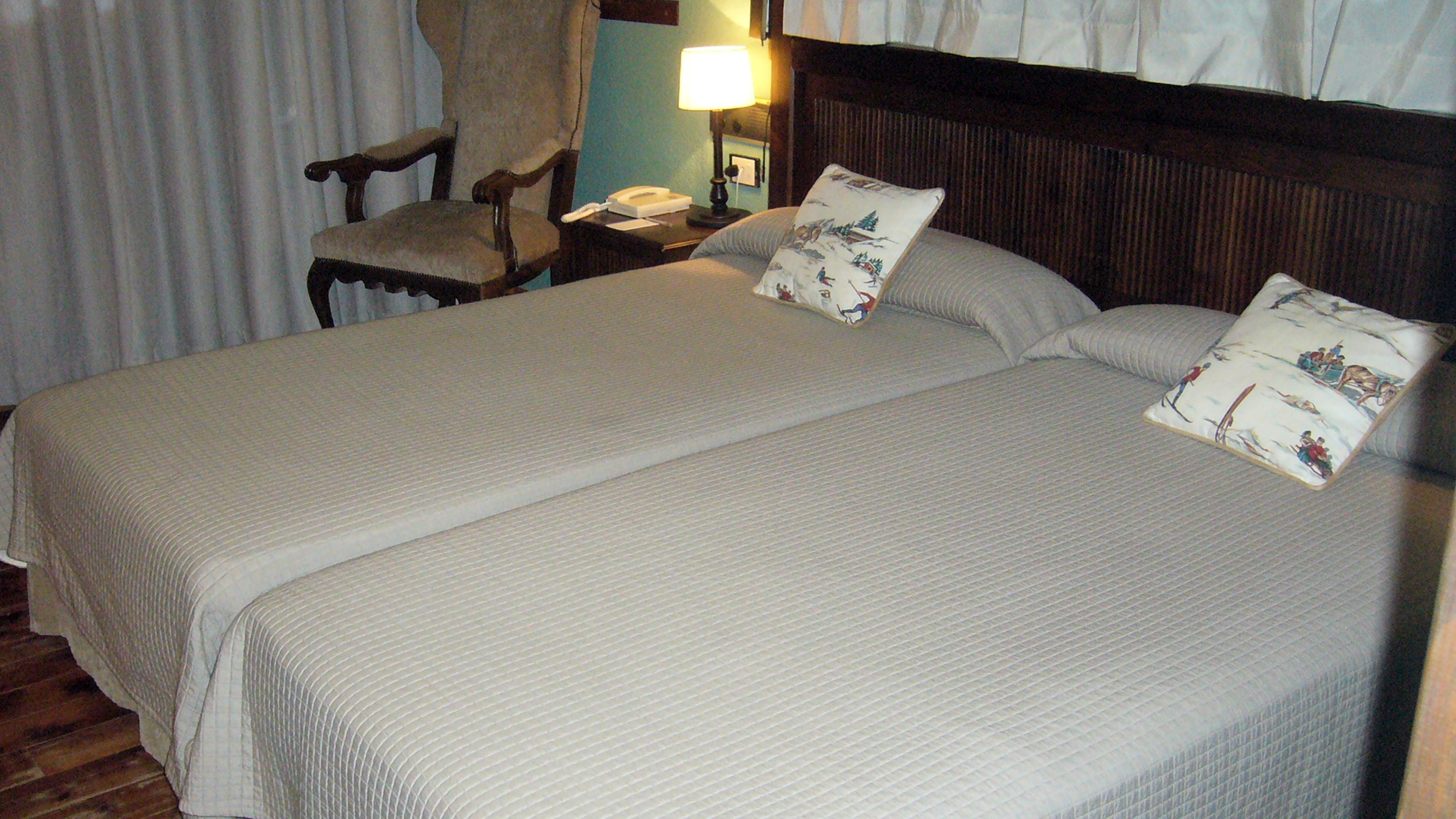 A double bed with a wooden headboard, two bedside tables, a chair, and a lamp.