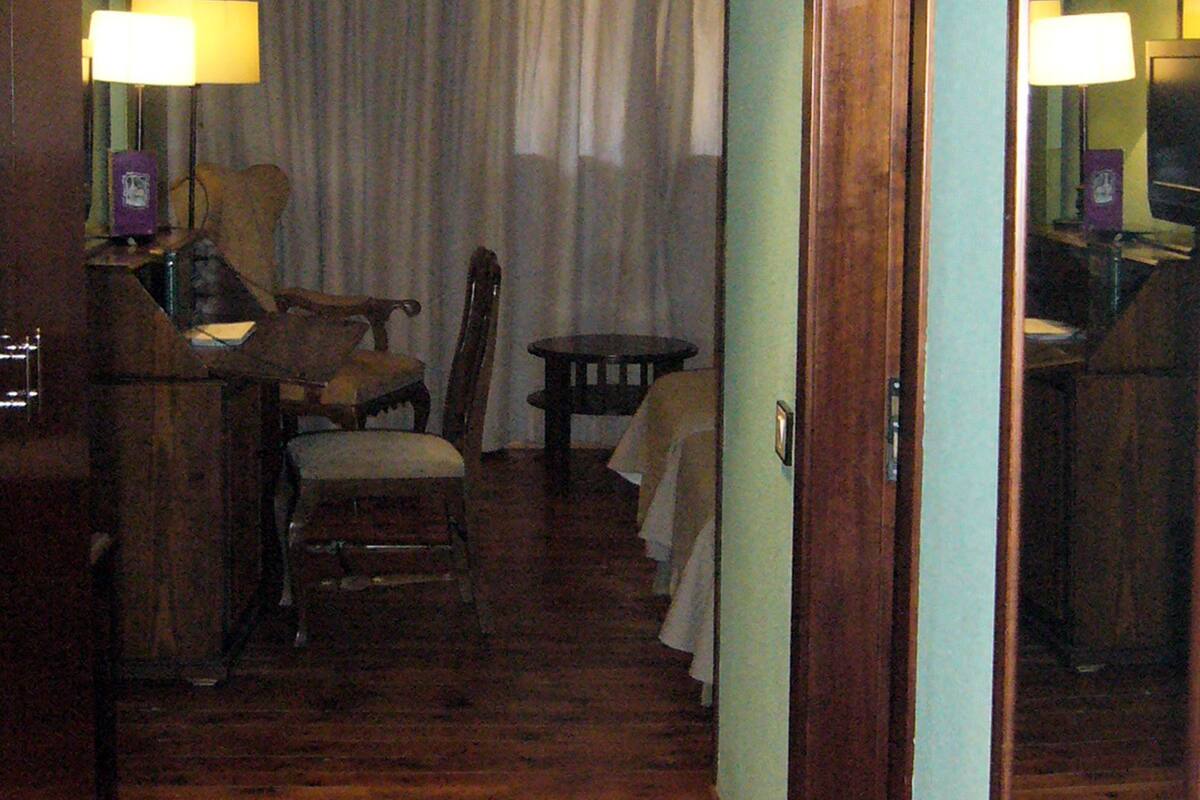 A hotel hallway with wooden flooring, a dining area with a table and chairs, and a large mirror on the wall.