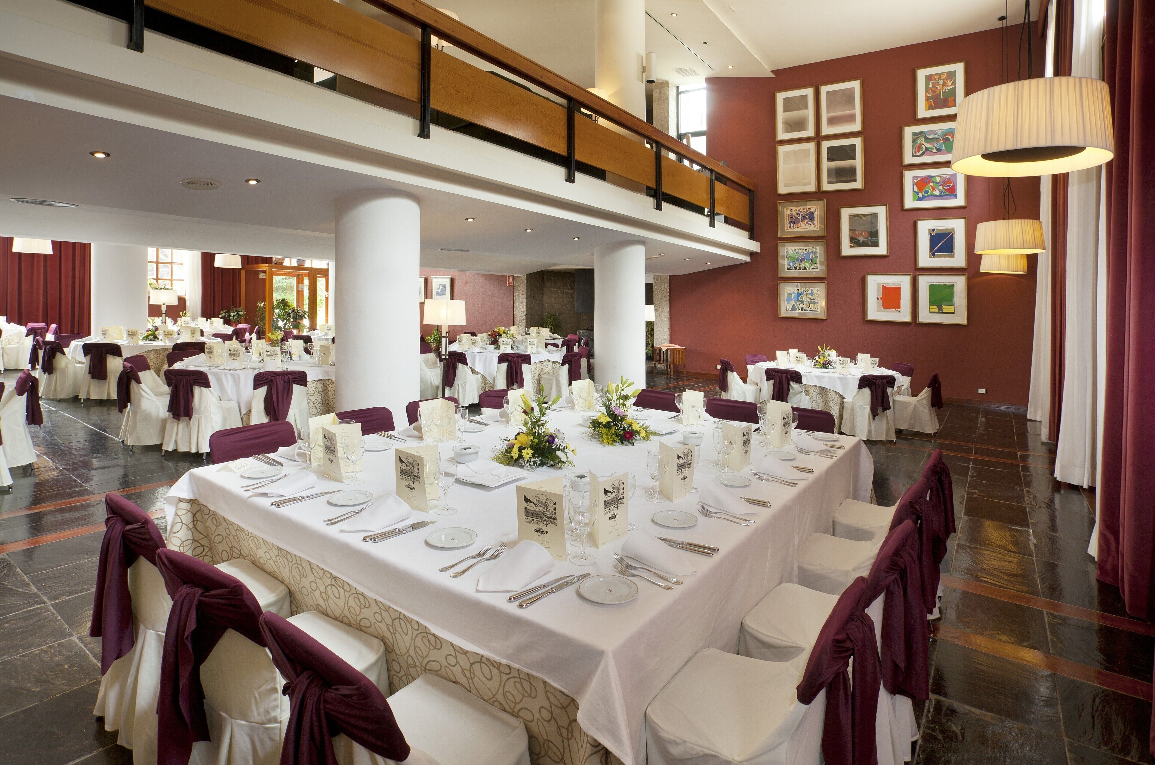 A spacious banquet hall with multiple round tables, each set with white tablecloths, silverware, and floral centerpieces.