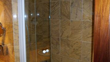 A bathroom with a glass-enclosed shower, marble tiles, and a wooden door.