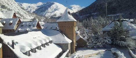 Un pueblo cubierto de nieve con edificios tradicionales, incluyendo una torre, y montañas al fondo.