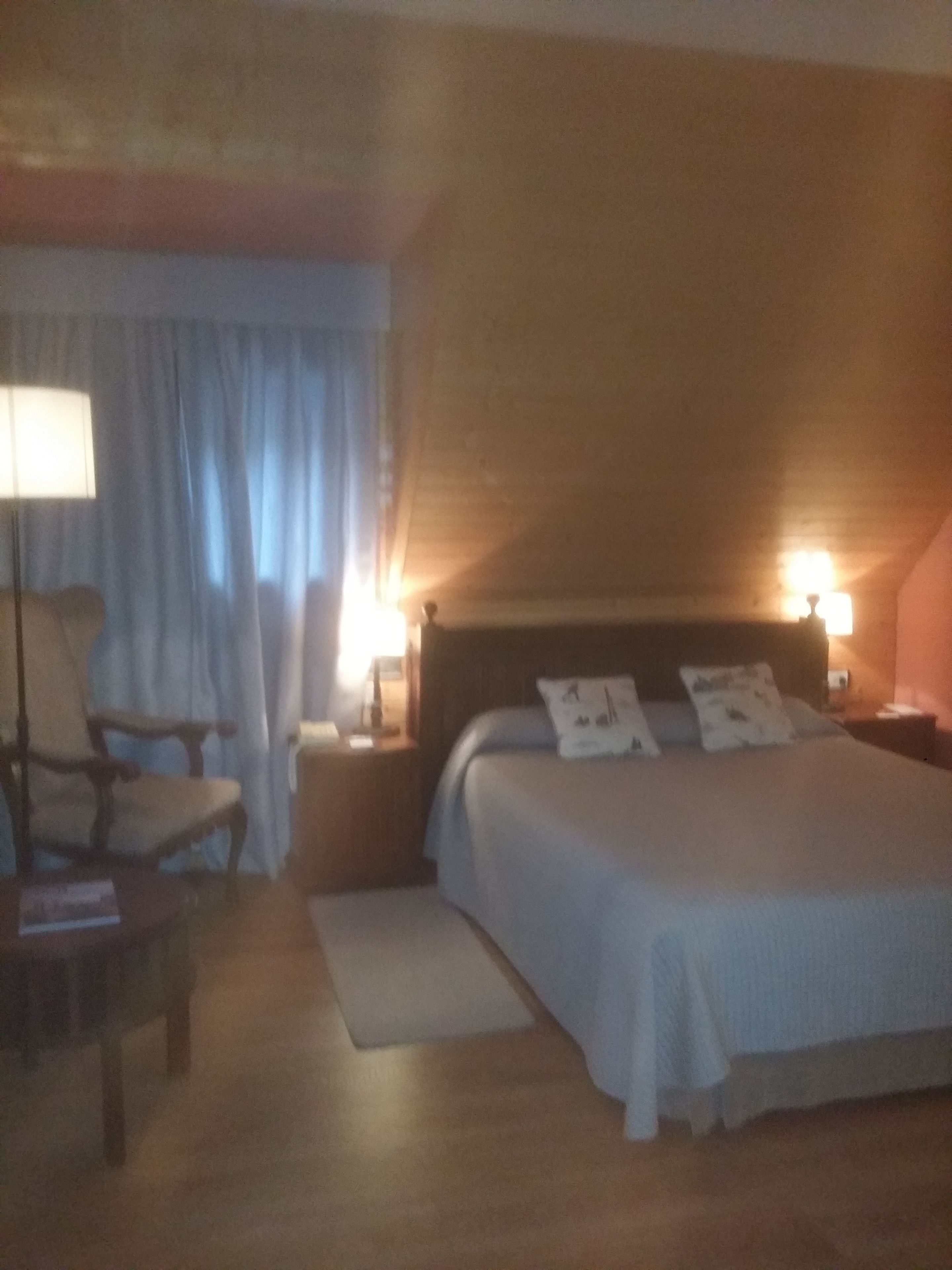 A bedroom with a bed, nightstands, a chair, a lamp, and curtains.
